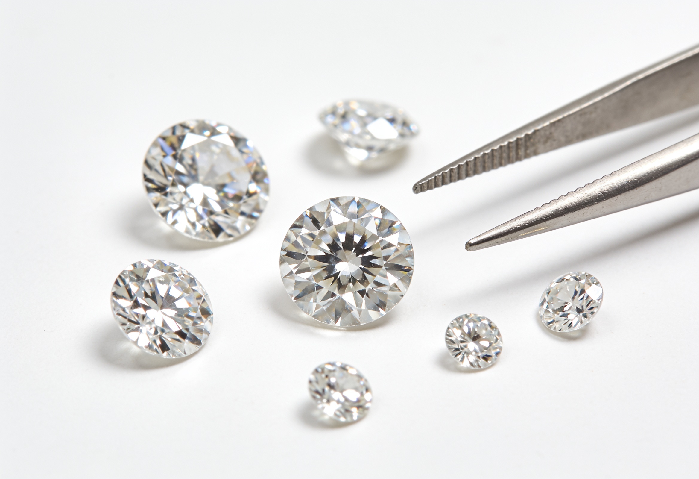 Loose round brilliant lab grown diamonds beside jeweler's tweezers